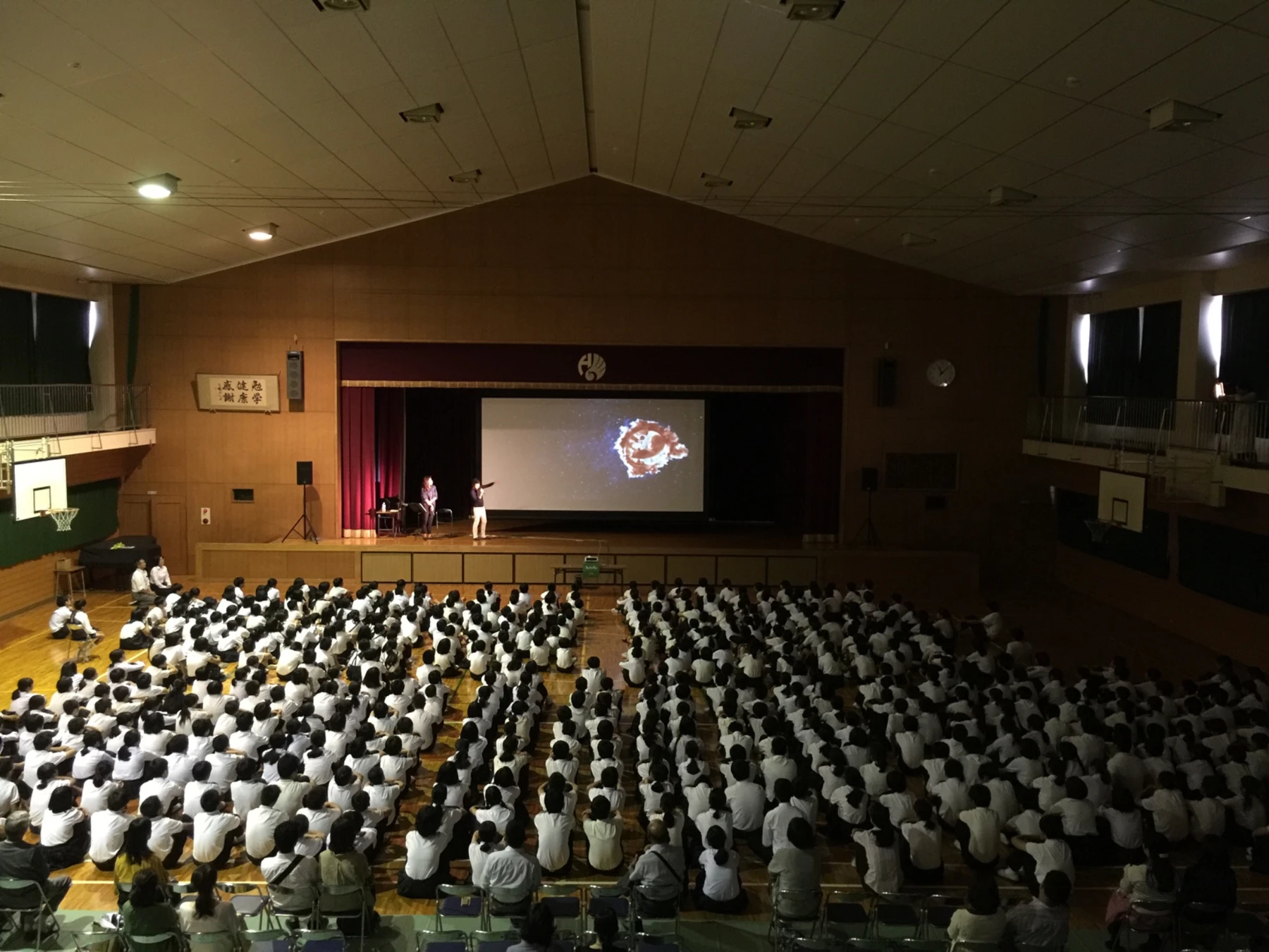 Students watching LIFE and a talk on a screen set up in their gymnasium